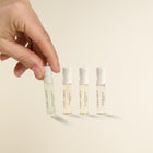 Hand holding a small bottle of Laura Ashley perfume with other bottles in the background on a beige background